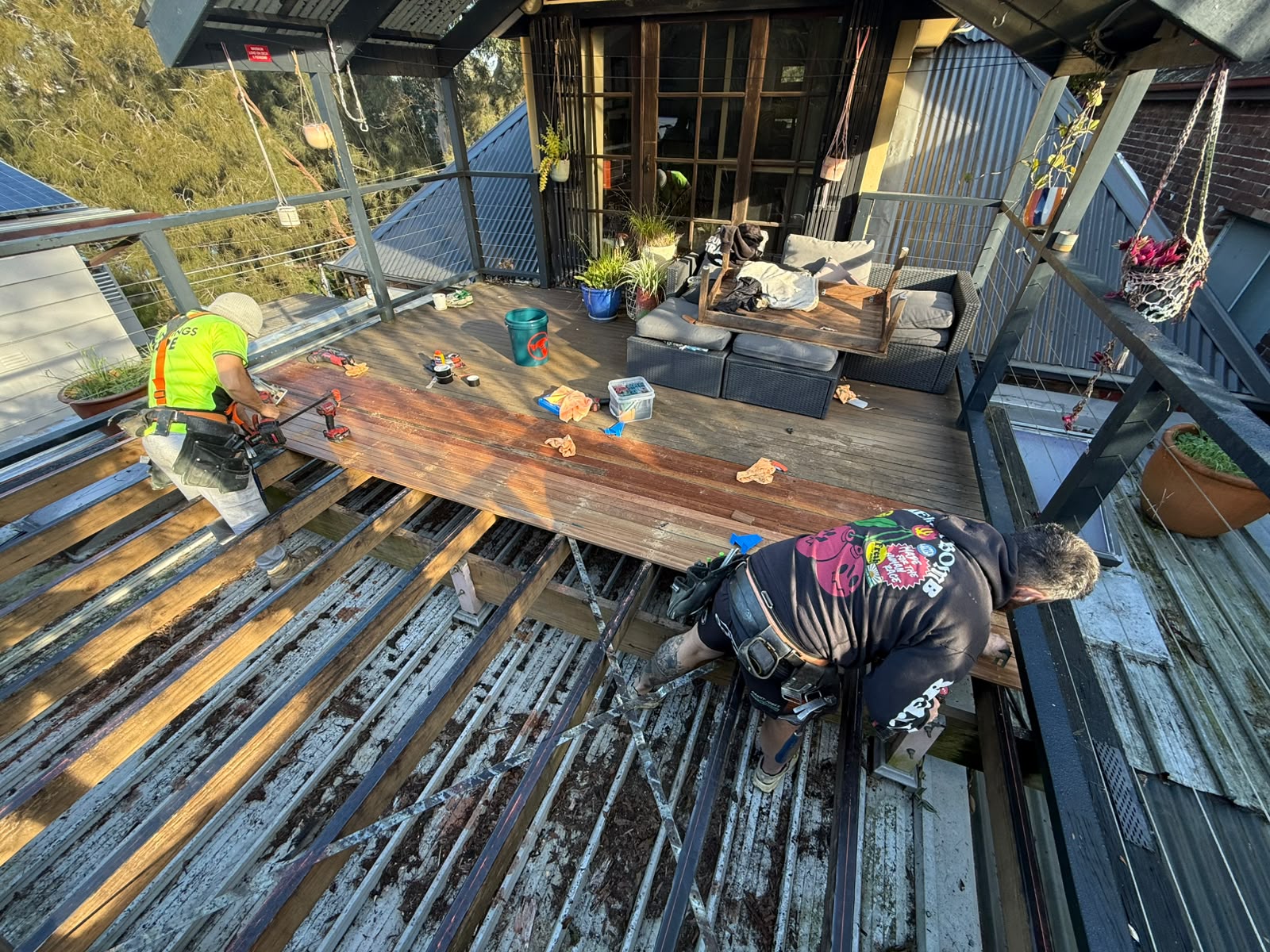 Two tradies relaying hardwood deck boards over a steel frame on a rear entertainer deck